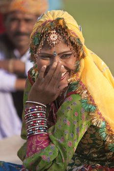 Indian lady in traditional costume covering her face and laughing at the annual elephant festival in Jaipur, Rajasthan, India.