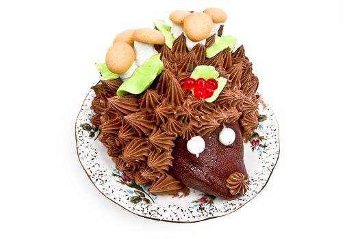 Cake in the form of a hedgehog, adorned with green leaves with cream, mushrooms from the biscuit and meringue, berries, jelly on a plate isolated on a white background