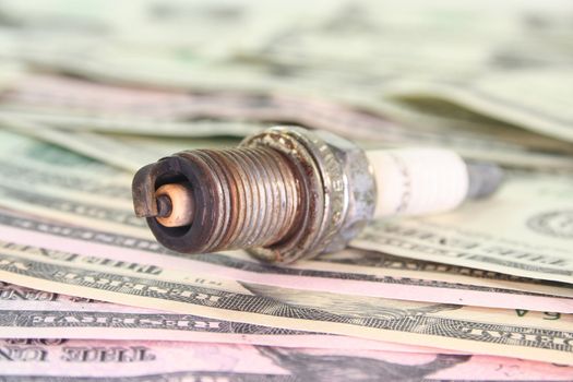 old rusty spark plug on many dollar bills