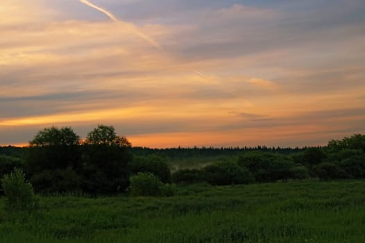 A beautiful sunrise, clouds, painted in red and orange colors, the trees in the meadow, the morning mist