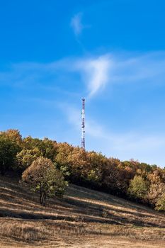 Holm, yellow and brown trees, tower communications on a background of blue sky and white clouds