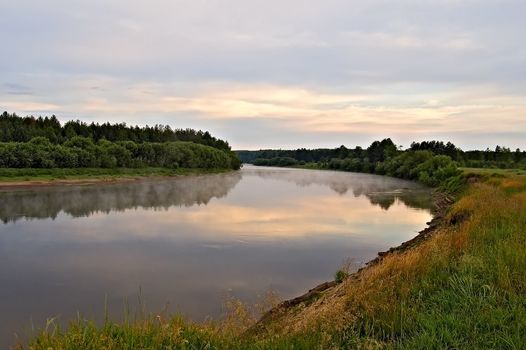 A beautiful sunrise on the river Sosva in the Northern Urals, clouds, painted in red, orange, forest, coast and their reflection in the river