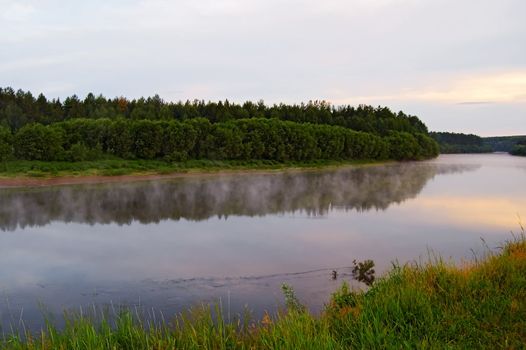 A beautiful sunrise on the river Sosva in the Northern Urals, clouds, painted in red, orange, forest, coast and their reflection in the river