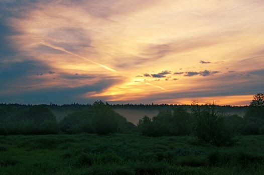 A beautiful sunrise, clouds, painted in red and orange colors, the trees in the meadow, the morning mist