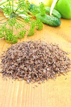 Dill seeds on a wooden board against the background green stalks of dill, cucumbers, beans and sweet peppers