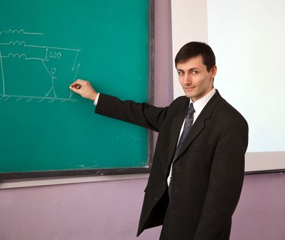 Young scientist giving a lecture on the background of the chalkboard with the scheme.