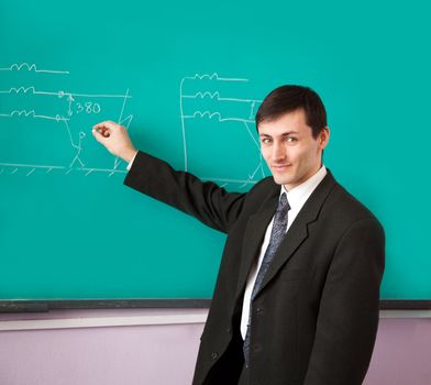 Young scientist giving a lecture on the background of the chalkboard with the scheme.
