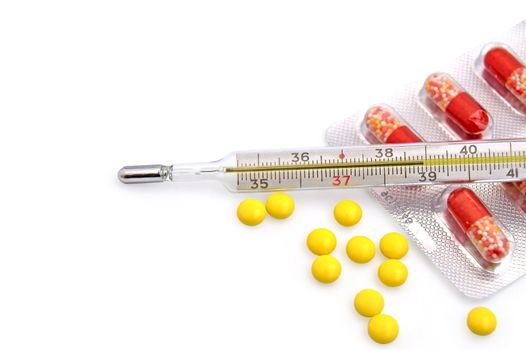 Thermometer with the yellow pills in bulk and red-white capsules in a package on a white background