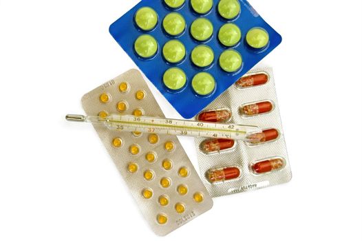 Thermometer with multi-colored pills and capsules in containers on a white background