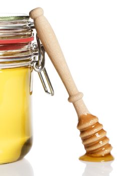 honey covered honey dipper leaning at a honey jar on white background