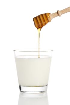 honey falling from a honey dipper in a glass of milk on white background