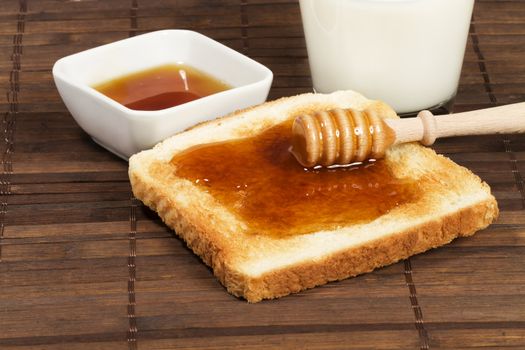 honey with honey dipper on a toast with a glass of milk and a jar with honey