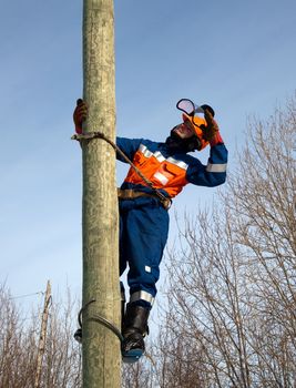 Electrician on the post against the blue sky