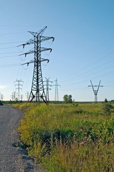 Mounts Electric Power lines against the blue sky, green grass and the dirt road