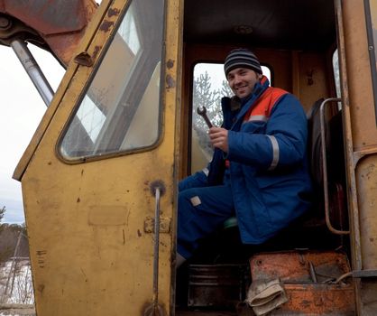 Machinist excavator with spanner in hand in the cab