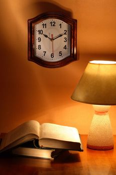 Still life with luminous desk lamp near old books and clock