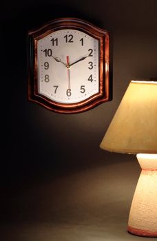 Still life with luminous desk lamp near clock on dark background