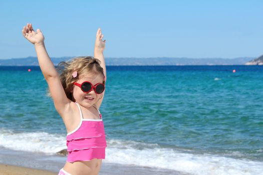 happy little girl with sunglasses and hands up on the beach