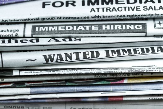 stack of newspaper with Classified ads,immediate hiring,wanted signs.