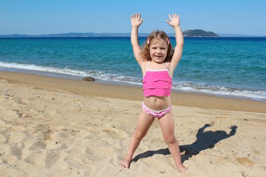 little girl with hands up standing on the beach