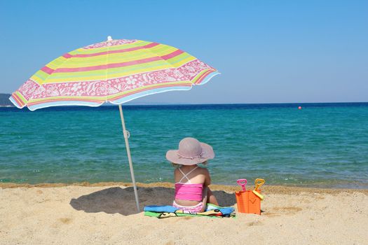 little girl sitting on beach under sunshade