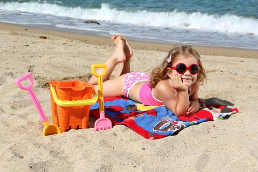 little girl with sunglasses lying on the beach