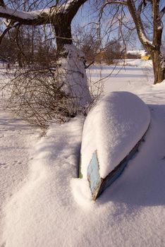 Boat near the tree covered by winter snow on the coast of the river.