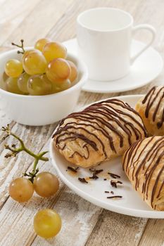 mini chocolate croissants, grapes and coffee cup on a rustic wood table