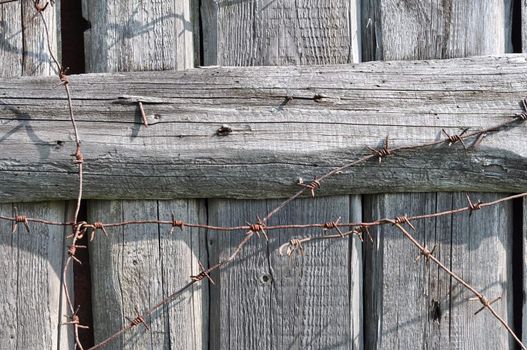 Old board fence with rusty nails and a barbed wire