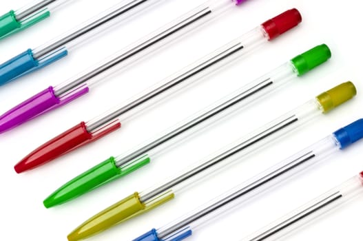 A selection of writing pens in a variety of colours arranged diagonally and over whtie