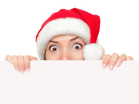 Christmas sign woman peeking over empty blank paper sign wearing santa hat isolated on white background. Funny surprised and shocked look on santa girl face.