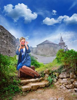 young woman dressed in retro style with an old suitcase on step stone staircase in the ruins of the ancient cave city
