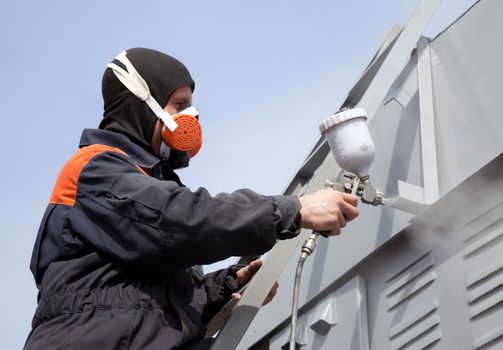 A commercial painter on the stairs spray painting a steel exterior wall against the blue sky