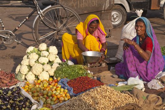 Indian women in brightly colored saris selling fruit and vegetables by the side of the road in Jaipur, Rajasthan, India.