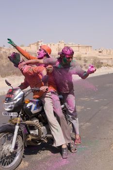 Group of young Indians on a motorbike covered in colored paint from celebrating the Hindu Festival of Holi outside Amber Fort in Jaipur, Rajasthan, India.