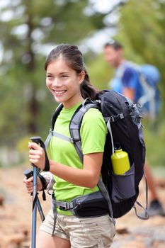 Hiking woman happy outdoors on hike in forest. Hiker in the background. Sporty active Asian Caucasian mixed race young woman smiling holding hiking sticks. Tenerife, Canary Islands, Spain