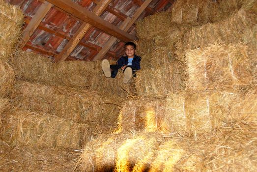boy sitting on straw bales in warehouse under roof