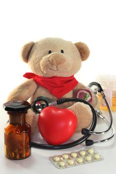 Teddy with a stethoscope and medication before a white background
