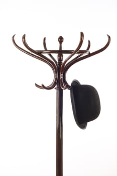 Bowler hat hangs on vintage wooden coat rack over white