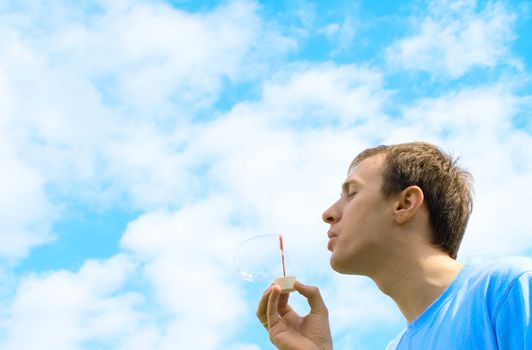 The young man starts up soap bubbles against the blue sky