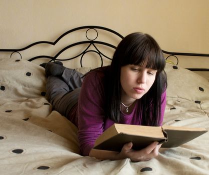 The young woman reads the book lying on a bed