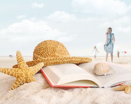 Straw hat , book and seashells on the beach with people walking