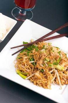 A Thai dish of stir fried chicken vegetables noodles jasmine rice and bean sprouts on a large white plate with chop sticks.