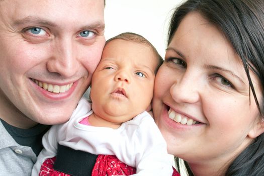 A young happy and healthy family  holding their newborn daughter between their cheeks.
