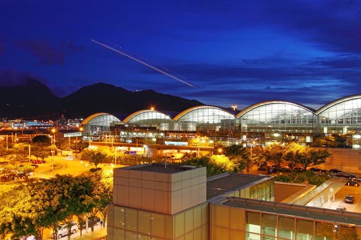 Modern architecture of airport exterior, together with flying plane at night.