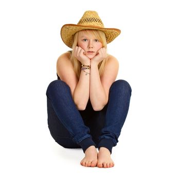 A young blonde in a straw hat sitting on the floor isolated on white background