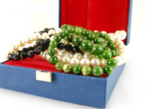 Green emerald gemstone over white and black pearl necklace, in a jewelry box, isolated towards white background