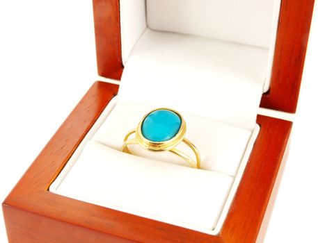 Blue gemstone on gold ring in a wooden box, isolated towards white
