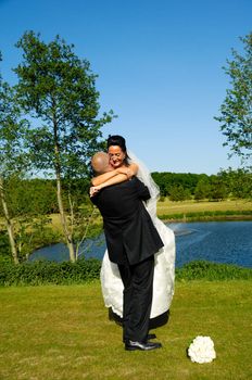 Groom is lifting his bride up in a park.