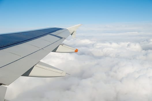 Wing and white clouds taken form above while flying in a plane.